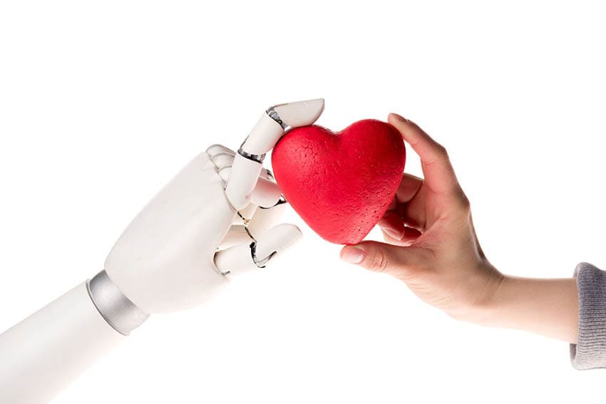 En robothand och en mänsklig hand håller i ett rött hjärta